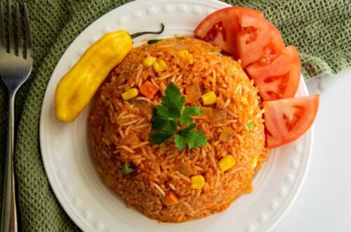 Jollof Rice on a white plate with tomatoes and a chilli pepper
