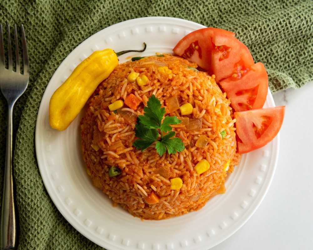 Jollof Rice on a white plate with tomatoes and a chilli pepper